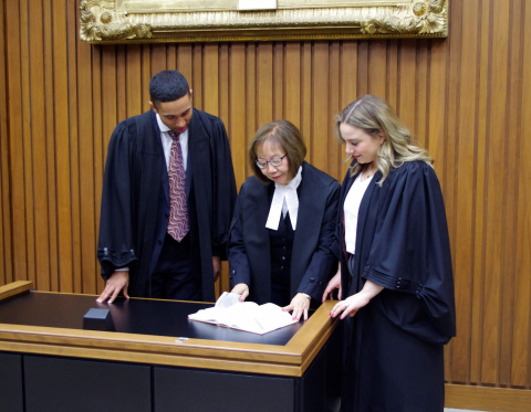 Young male and female law clerks review legal papers with a female judge. They are all wearing black robes.  