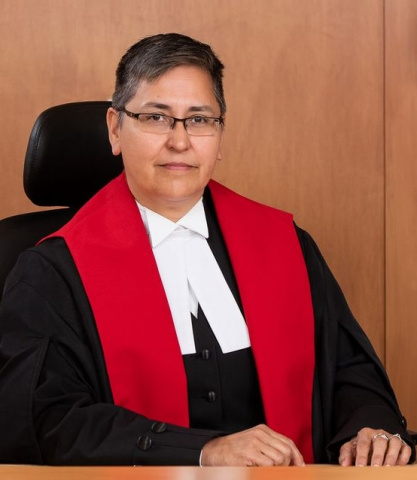 Indigenous woman with glasses and short hair wearing black, red and white judicial robes.