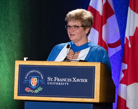 Female judge standing in front of a podium with a Canadian flag behind her.