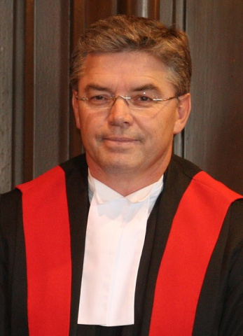Man wearing glasses and red, black and white judicial robes. 