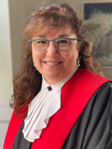 Woman with long curly brown hair and glasses in red, black and white judicial robes. 