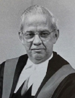 Black and white photo of a male judge in robes. 