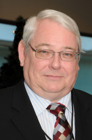 Man with white hair and glasses wearing a suit and checkered tie. 