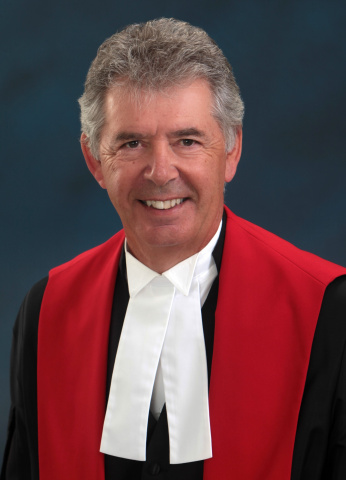 Man with salt-and-pepper hair wearing red, black and white judicial robes. 