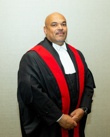 Black male judge wearing black judicial robes with a red sash.  