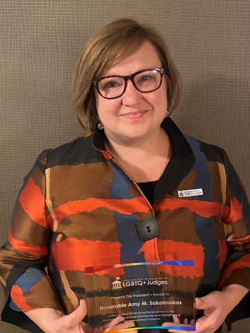 Female with short hair wearing glasses and a colourful top, holding a glass award. 