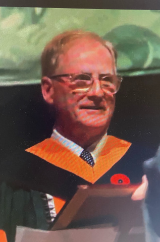 Smiling man in glasses wearing a orange, black and white robes. 