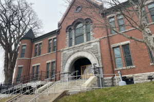 Large red brick courthouse with a stone staircase leading to the front entrance. 