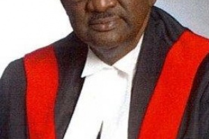 Bald black man with glasses wearing red, white and black judicial robes. 