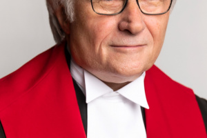 Man with gray hair and glasses in red, black and white judicial robes. 