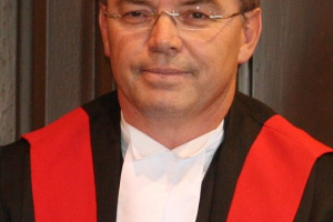 Man wearing glasses and red, black and white judicial robes. 