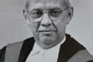 Black and white photo of a male judge in robes. 