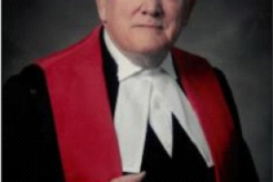 Grey-haired man wearing red, white and black judicial robes. 