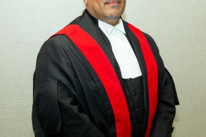 Black male judge wearing black judicial robes with a red sash.  