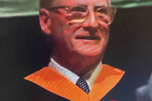 Smiling man in glasses wearing a orange, black and white robes. 